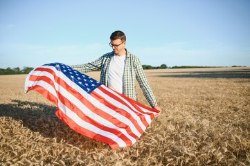 Young man holding American flag, standing in wheat field