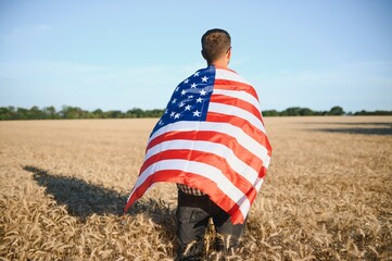 Young man holding American flag, standing in wheat field