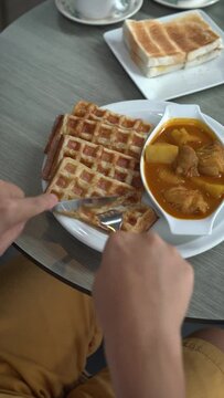 Man slicing and eating delicious waffles with curry chicken in a restaurant. Yummy fusion asian-western style food. 