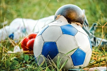 Burst soccer ball lies in pile of garbage on green grass in city. Torn ball thrown as rubbish after...