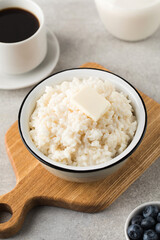 Rice porridge or pudding with a piece of butter, a mug of coffee and blueberries in a bowl. Healthy breakfast.