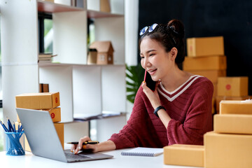 Online business owner Asian woman answering the phone talking to a customer and take note of the...