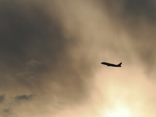 太陽に照らされた雲を背景にして上昇してく飛行機のシルエット