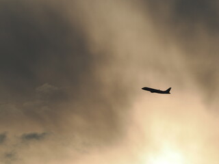太陽に照らされた雲を背景にして上昇してく飛行機のシルエット