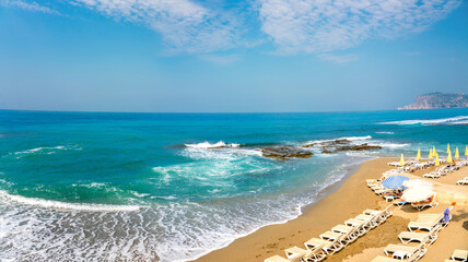 Beautiful curved line of turquoise sea surf with foam and rocks on sandy beach of a mediterranean resort.