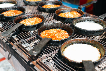 Draniki is popular dish of European cuisine. Row of cooking potato pancakes in frying pan on grill outdoors. Close-up, selective focus