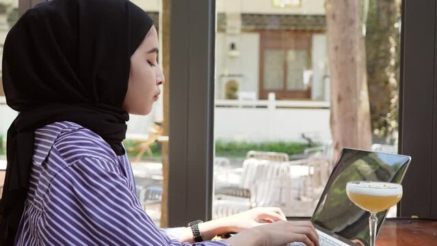 A Young Muslim Woman Typing On His While Giving Slight Smile At The End