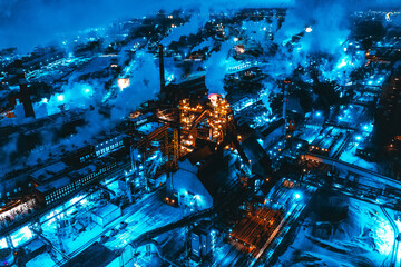 Aerial view of steel plant at night with smokestacks and fire blazing out of the pipe. Industrial panoramic landmark with blast furnance of metallurgical production. Concept of environmental pollution