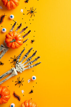 Halloween concept. Top view vertical photo of skeleton hands holding pumpkins spiders centipedes spooky eyes and confetti on isolated orange background