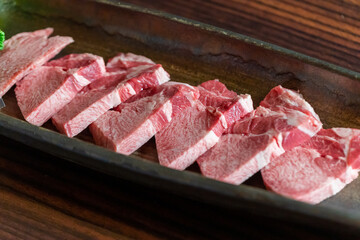 美しいサシが入り、一頭からわずかしか取れない希少な部位を贅沢に厚切りした牛霜降り上タン元。とろけるような脂の質感が際立つ一皿で、高級焼肉の目玉や特別な宴会、御膳の販促に最適な高品質素材です。 | Freshly sliced premium beef tongue (Tan-moto) on a plate.