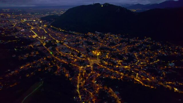 Aerial drone view of the Saint Nicholas Church in Brasov at night, Romania. Medieval church with multiple buildings and roads with nightlights