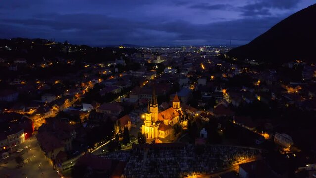 Aerial drone view of the Saint Nicholas Church in Brasov at night, Romania. Medieval church with multiple buildings and roads with nightlights