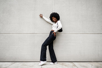 Black woman with afro hair posing in front of a gray concrete wall - Powered by Adobe
