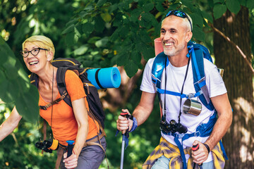 Senior couple hiking in forest wearing backpacks and hiking poles. Nordic walking, trekking....