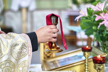 During the service, the priest raises the cup with wine. Religion. Eucharist.
