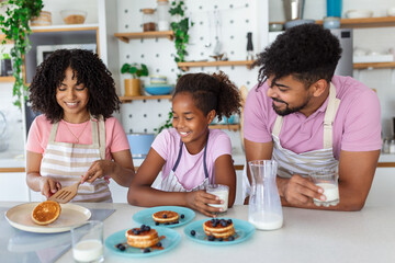 Preparing home bakery. Loving friendly afro american family spouses with daughter cooking food together at kitchen table, making homemade pancakes