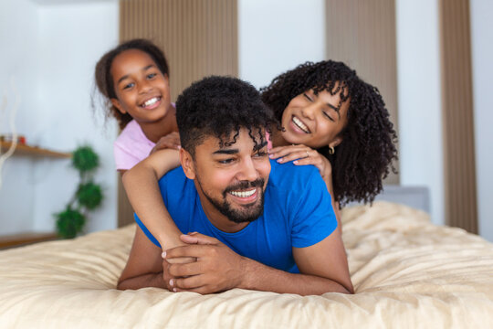 Smiling african american family of three lying on bed one on top,one in midlle and one in bottom.