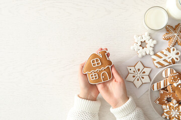 Woman holding delicious homemade Christmas cookie at white table, top view. Space for text