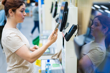Woman paying with smartphone in store at self-checkout counter.