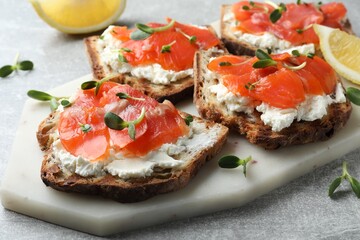 Delicious sandwiches with cream cheese, salmon and microgreens on light grey table, closeup