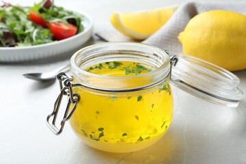 Jar with lemon sauce on light table, closeup. Delicious salad dressing