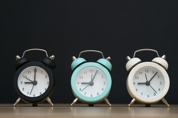 Three small alarm clocks black blue and white show nine o'clock, stand on a table on a black background