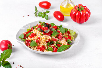 Warm salad with ptitim pasta, grilled peppers, tomato, arugula, basil and olive oil served on the white plate