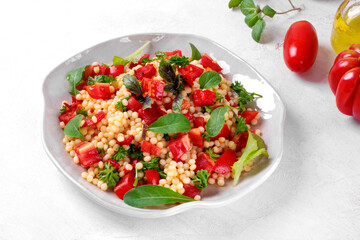 Warm salad with ptitim pasta, grilled peppers, tomato, arugula, basil and olive oil served on the white plate