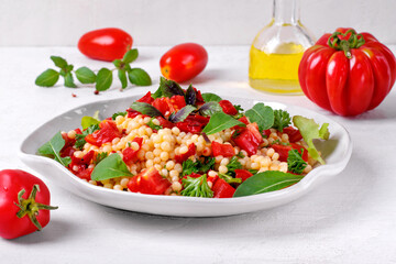 Warm salad with ptitim pasta, grilled peppers, tomato, arugula, basil and olive oil served on the white plate