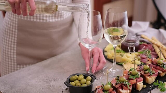 woman pouring wine to a glass from a bottle at domestic kitchen with meat and cheese plater on the table