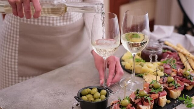 woman pouring wine to a glass from a bottle at domestic kitchen with meat and cheese plater on the table