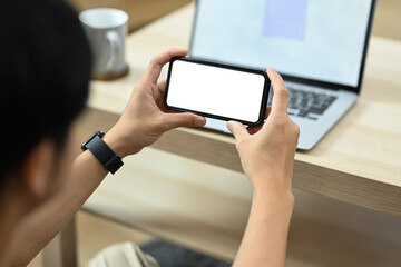 Man sitting in cozy living room and using smart phone. Over shoulder view.