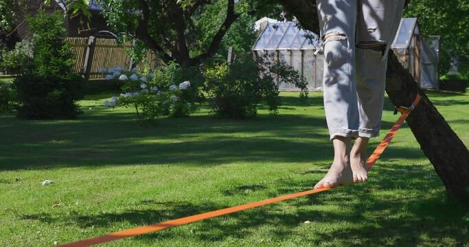 A person walking on slackline training balance with bear foot on a warm sunny summer day in a green garden. Healthy living concept.