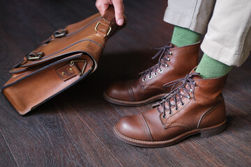 man in stylish boots takes a leather briefcase from a wooden floor before go for work