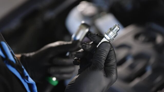 Male hand holds automotive spark plug. Close up of worker hands changes spark plugs in car engine in auto service. New spark plugs. Male auto mechanic changes spark plugs in a car engine