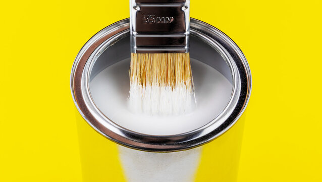 paint brush with white paint flowing into a can on yellow background close-up