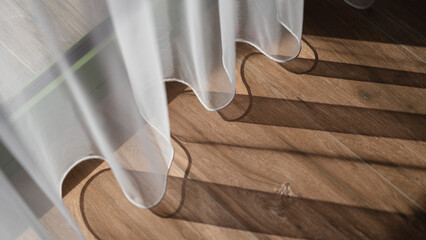 Closeup of light white curtains and brown wood laminate by window