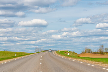Fototapeta premium Cars asphalt road through the green agricultural fields background on a sunny summer day.