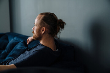 Young ginger man sitting on sofa while resting at home