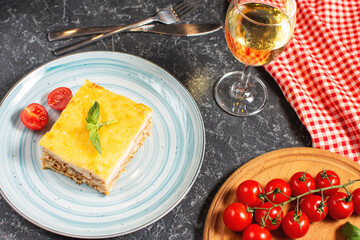 Delicious homemade italian Lasagna with bachamel sauce and glasses of wine on black stone background