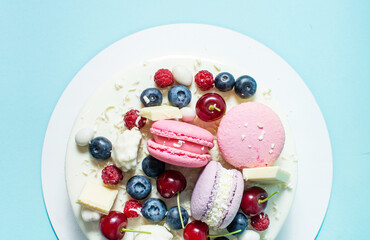 Tender white cake decorated with melted white chocolate, macaroons, berries and candies on blue background. Top view