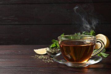 Glass cup of freshly brewed tea on wooden table. Space for text