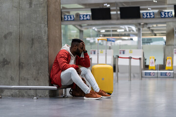 Sad African American man upset at airport his flight is delayed. Depressed traveler male waiting...