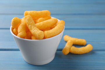 Many tasty cheesy corn puffs on blue wooden table