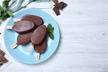 Flat lay composition with glazed ice cream bars, fresh mint and chocolate on white wooden table. Space for text