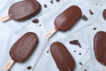 Glazed ice cream bars and chocolate chunks on light grey table, flat lay