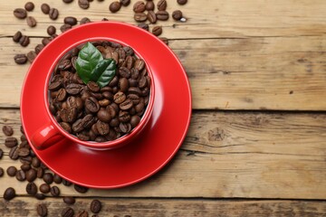 Red cup with roasted coffee beans and leaves on wooden table, flat lay. Space for text