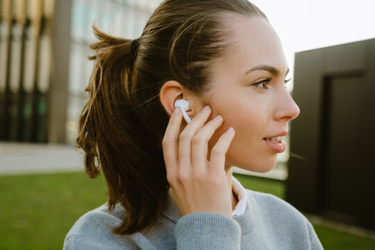 Young woman looking aside and listening music with earphones