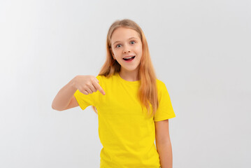 Enthusiastic teen girl smiling, pointing finger down, showing promo offer, way to store, banner or logo, standing in blank yellow tshirt over white background