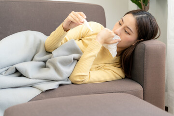 Asian woman sick at home. The woman had a cough, sore throat,runny nose and a high fever. patient with thermometer on sofa